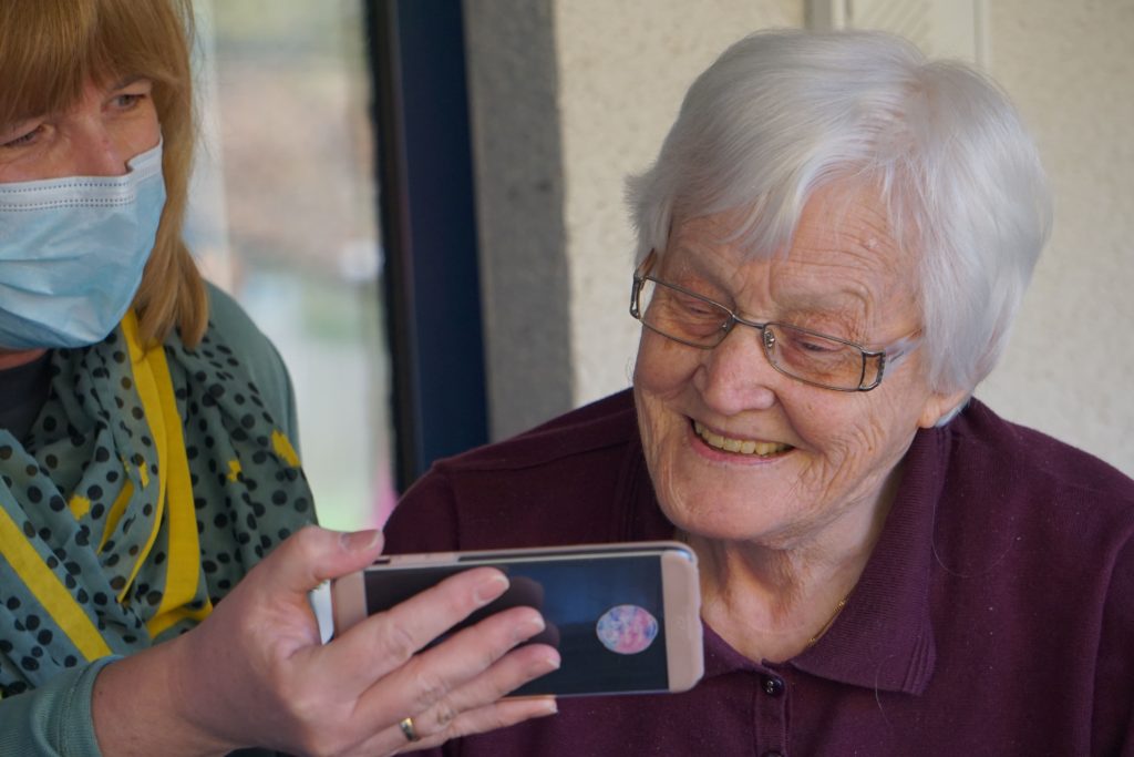 Old woman smiling at something being shown to her on a cell phone